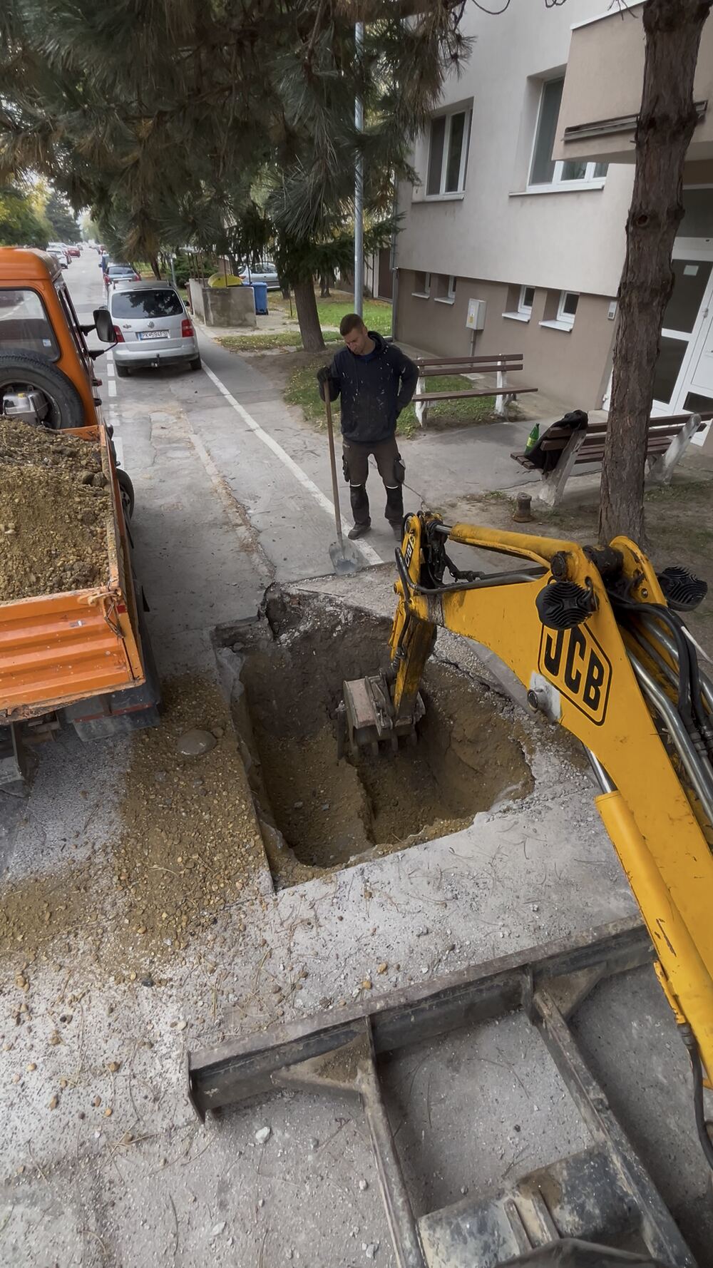 Minibager JCB kope jamu pri ceste, vedľa stojí sklápačka
